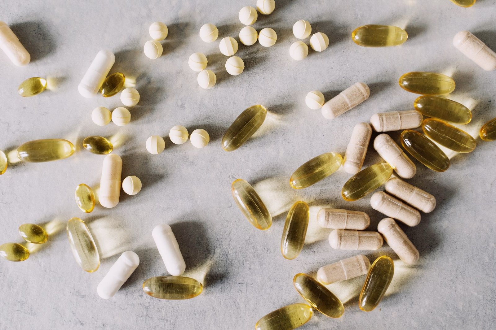 Vitamin tablets, capsules and fish oil softgels spread on a light stone surface