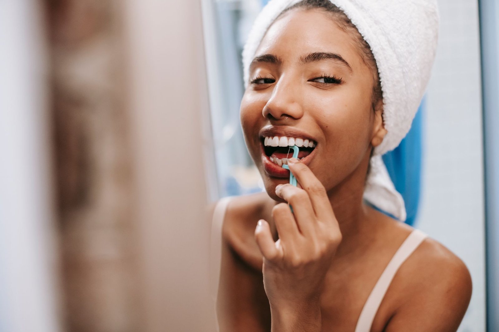 Woman using a dental flosser in front of a bathroom mirror