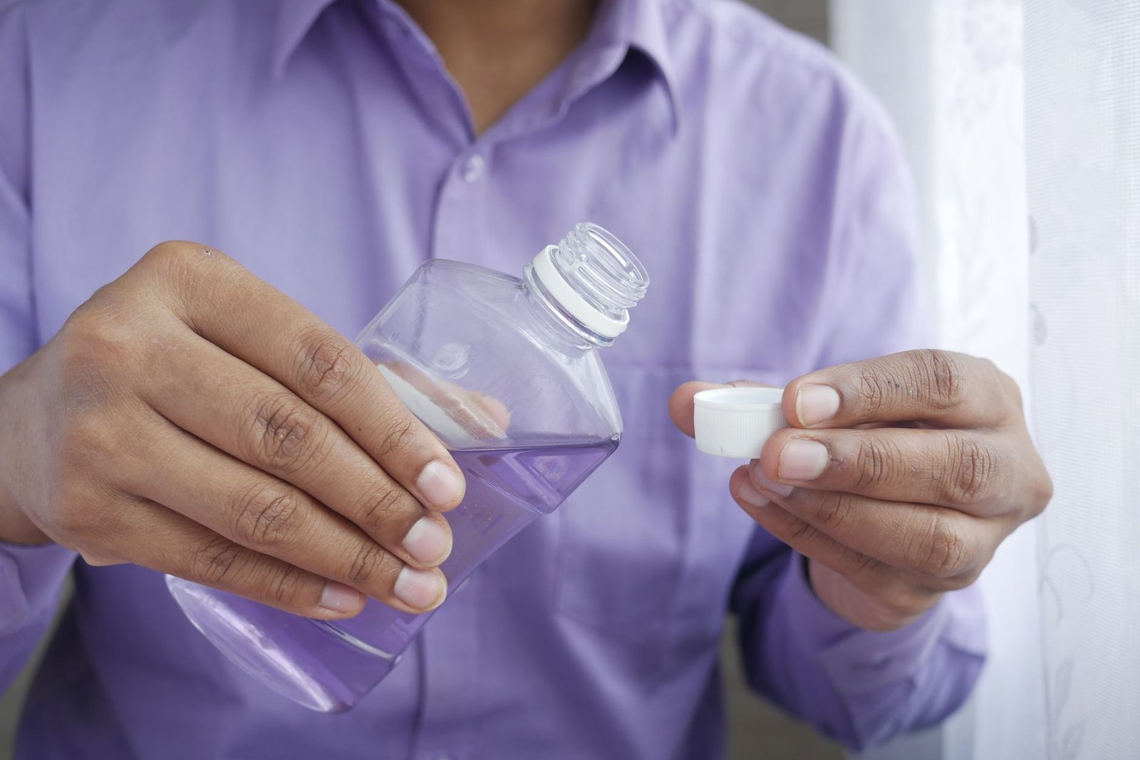 Hands pouring purple mouthwash from a clear bottle into the cap