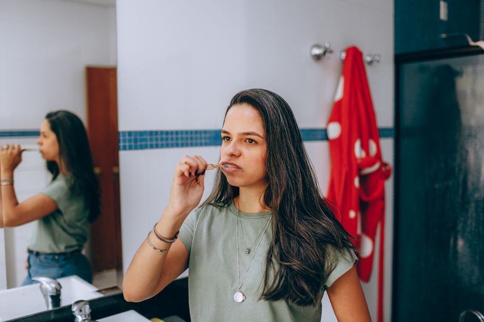 Woman brushing her teeth at a bathroom mirror as part of a daily oral care routine