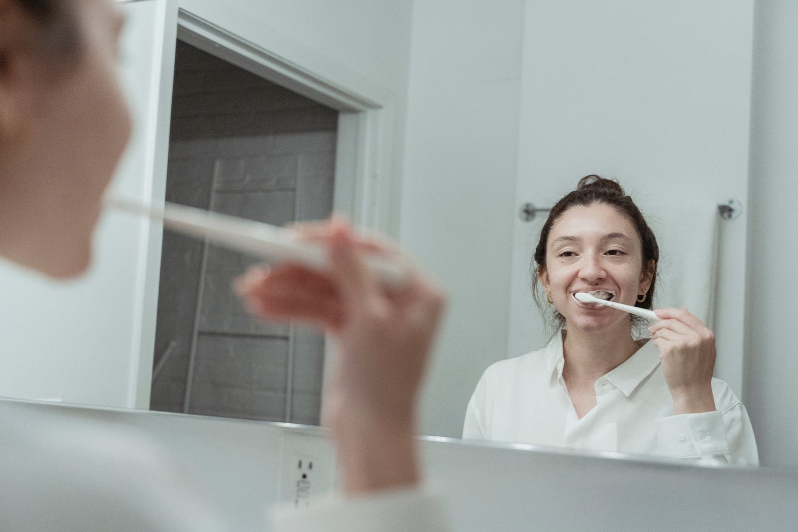 Woman brushing her teeth in front of a bathroom mirror