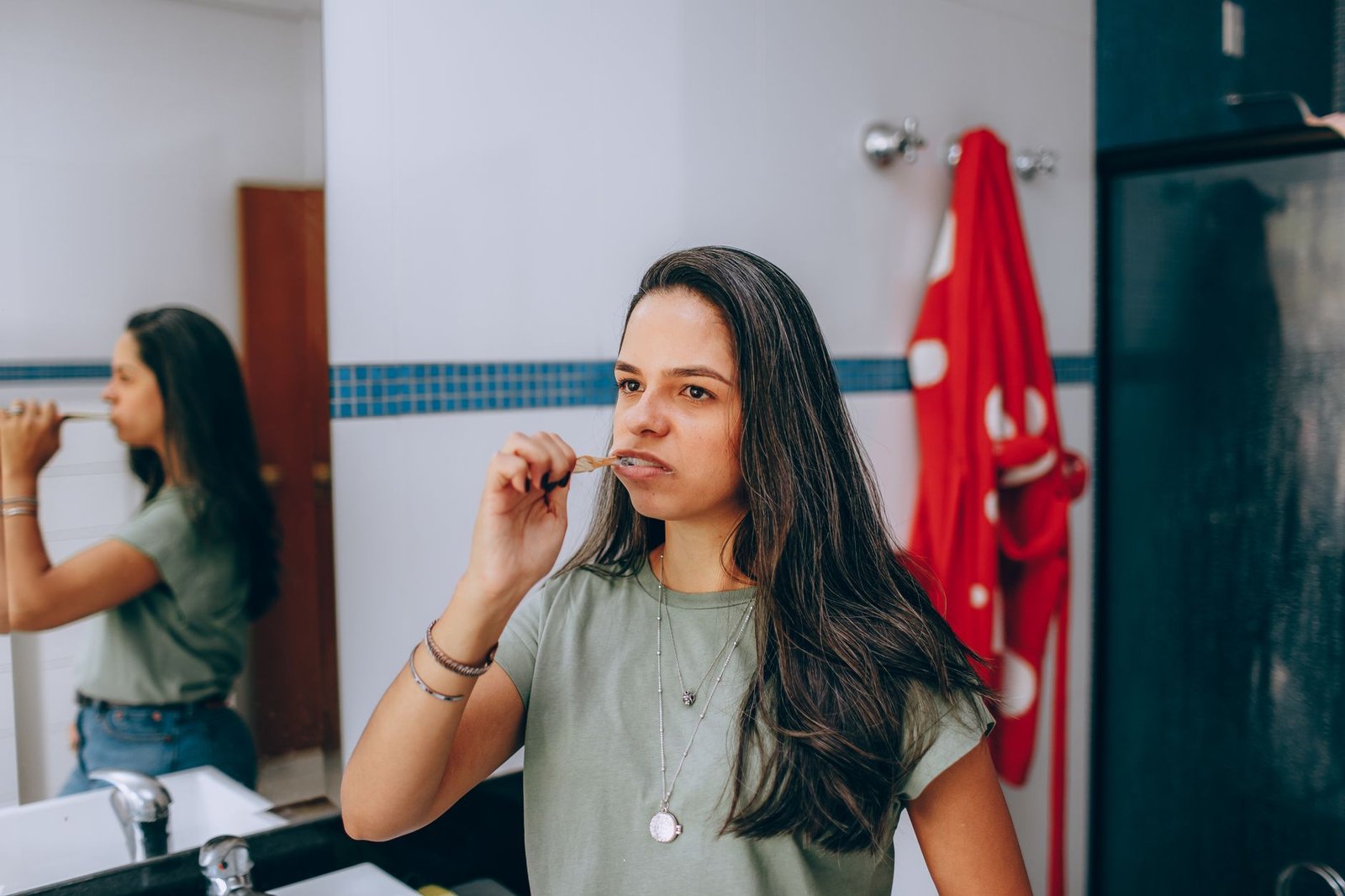 Woman brushing her teeth at a bathroom mirror as part of a daily oral care routine